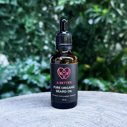 Bottle of 'A Better' pure organic beard oil on a wooden surface with a blurred green background