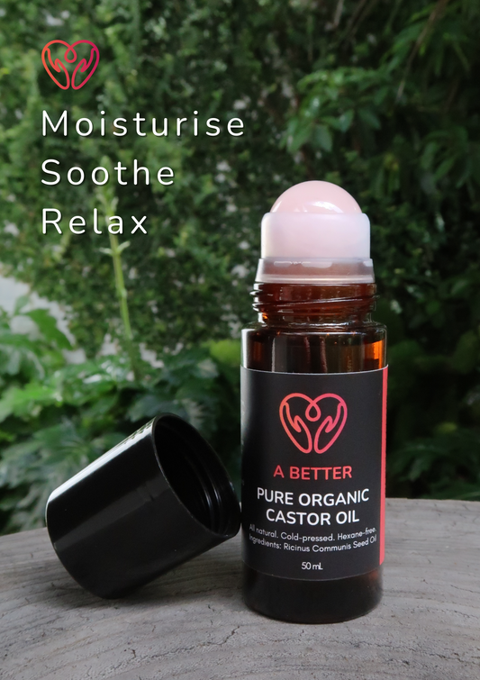 Bottle of A Better Pure Organic Castor Oil with a roller ball on a wooden surface with greenery in the background.