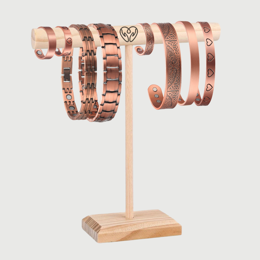 Set of pure copper bracelets on a wooden stand against a light gray background