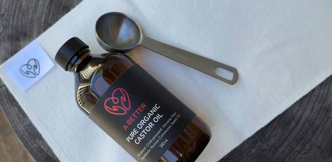 Bottle of A Better Pure Organic Castor Oil with measuring spoons on a castor oil wrap