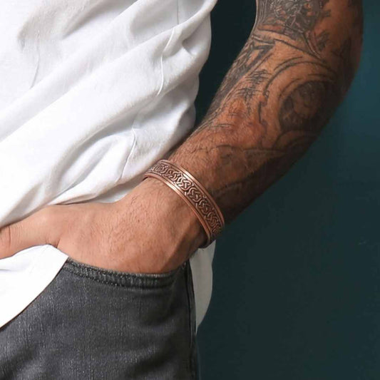 Person wearing a copper bracelet with intricate designs on a dark background